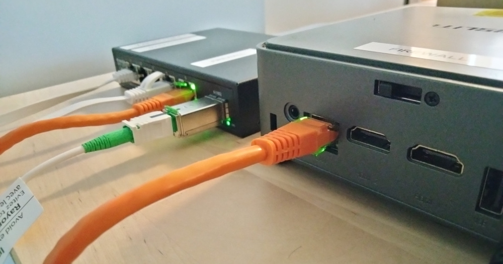 Photo of a mini PC and a network switch sitting atop a desk with various cables plugged into each unit